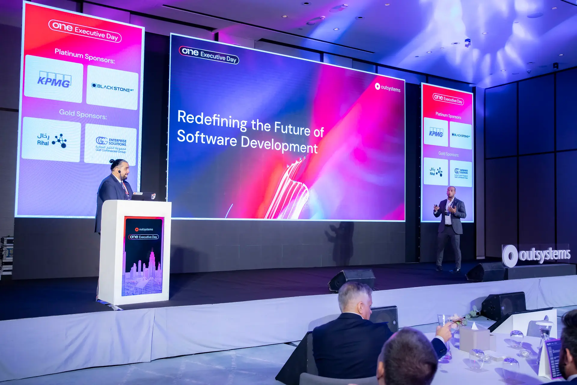 A speaker on the OutSystems stage beside a screen reading Redefining the Future of Software Development