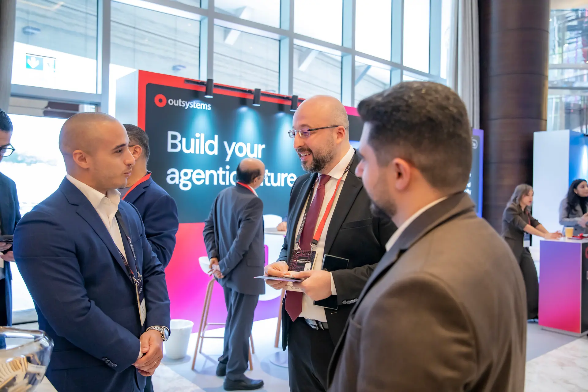 Delegates talking in small groups in front of an OutSystems Build your agentic future stand